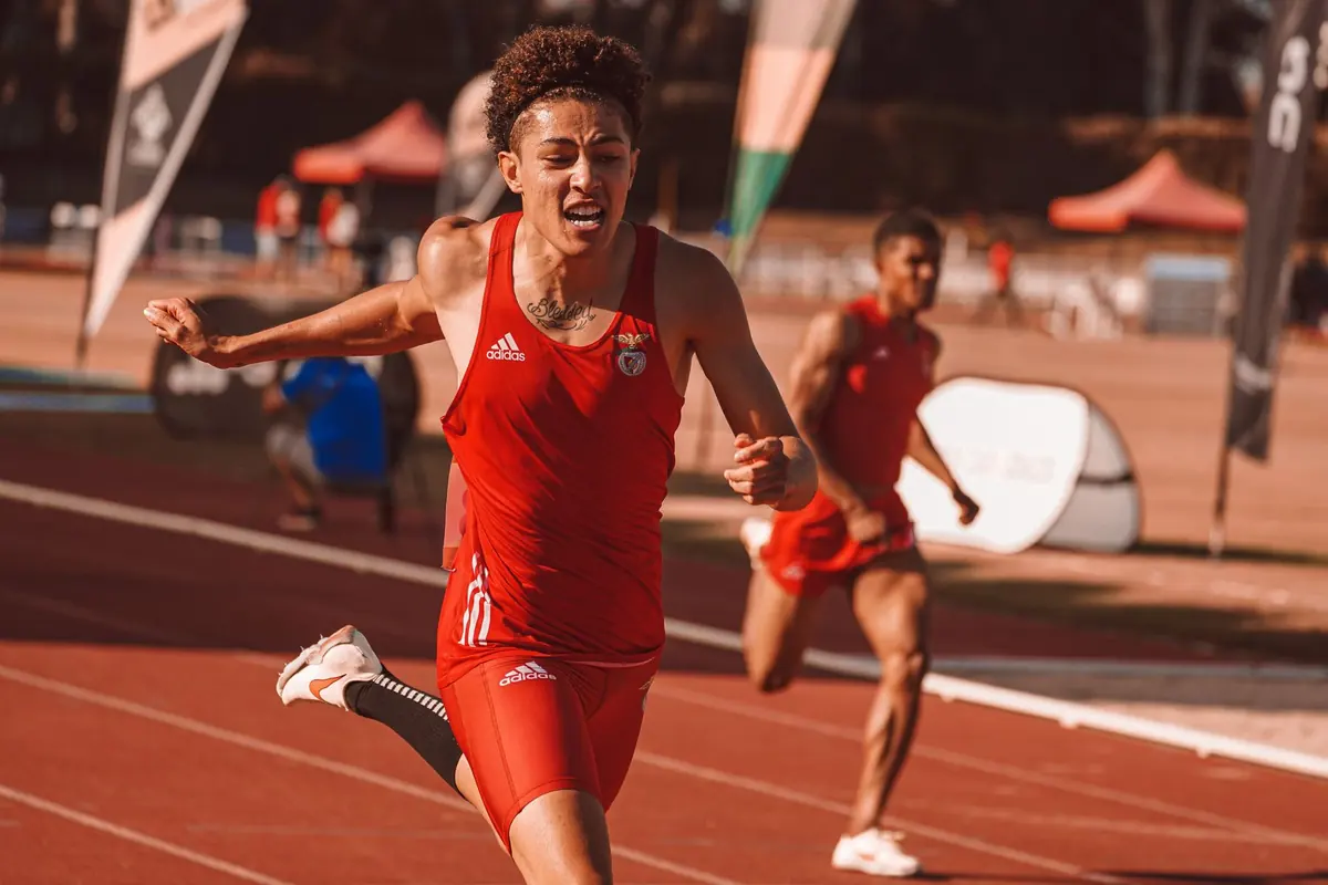 Kırmızı formalı bir atlet, atletizm pistinde koşarken