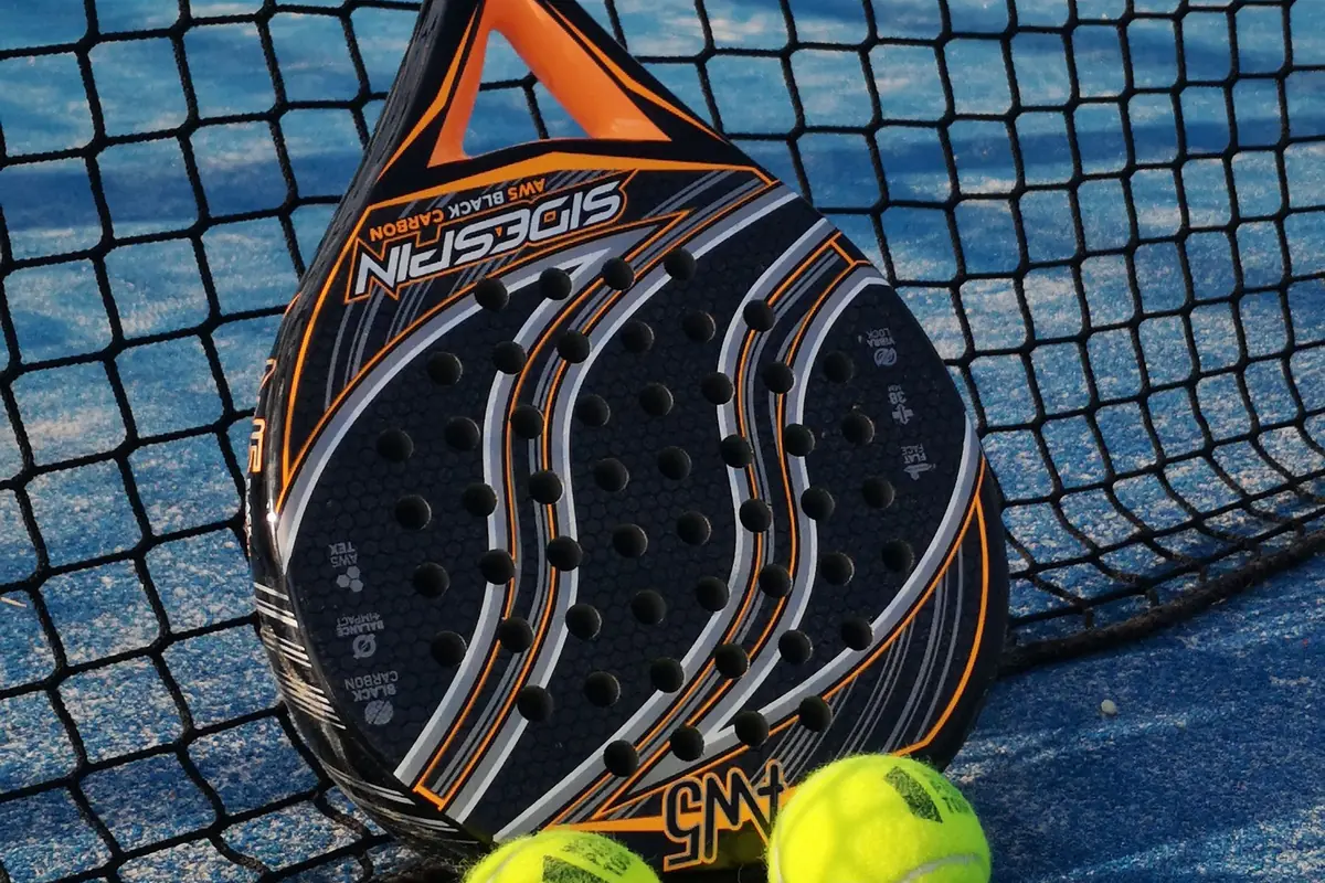 Bir padel raketi ve sarı toplar, filenin önünde