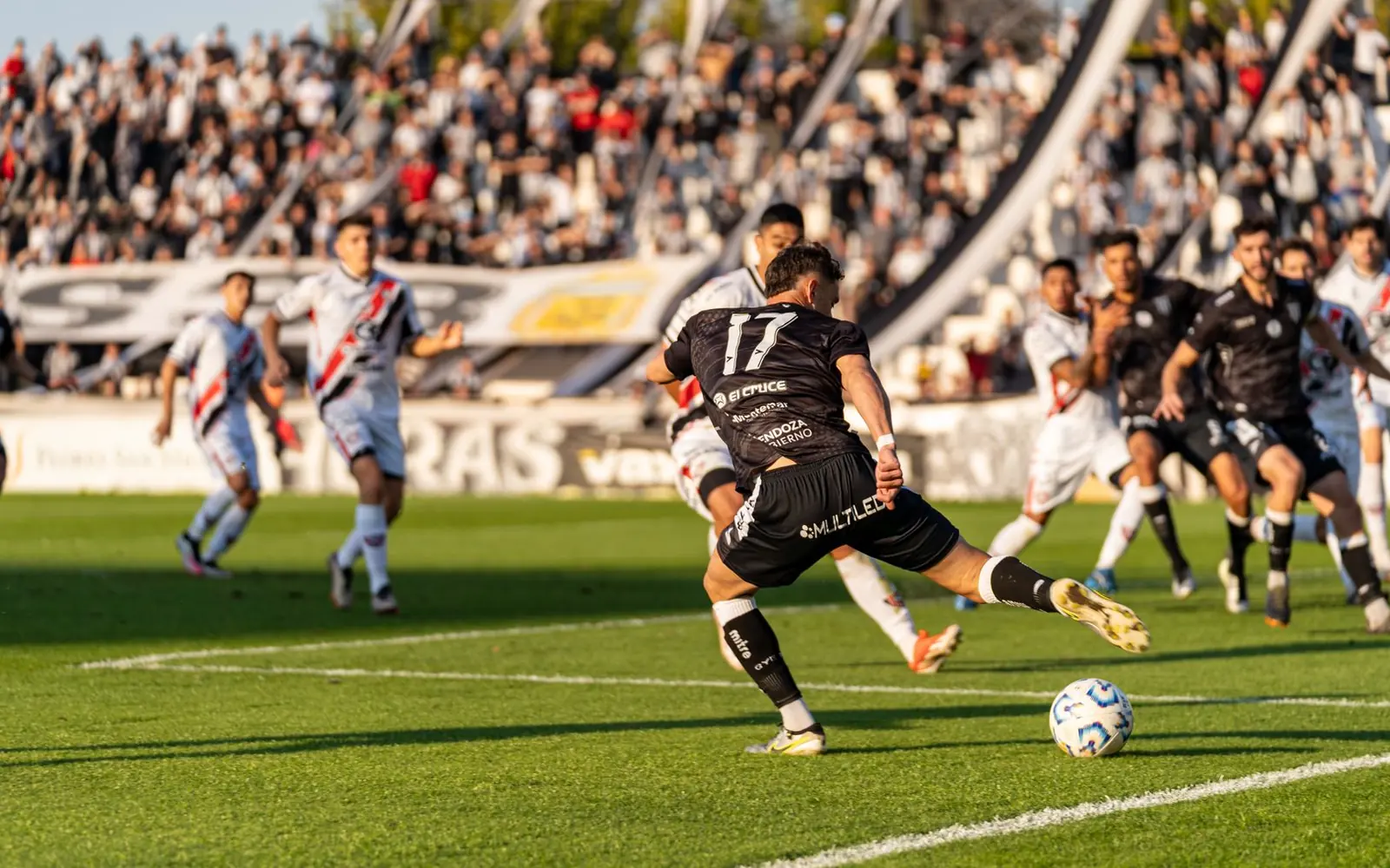 Dolu bir stadyumda oynanan futbol maçından bir an: oyuncular topun peşinde